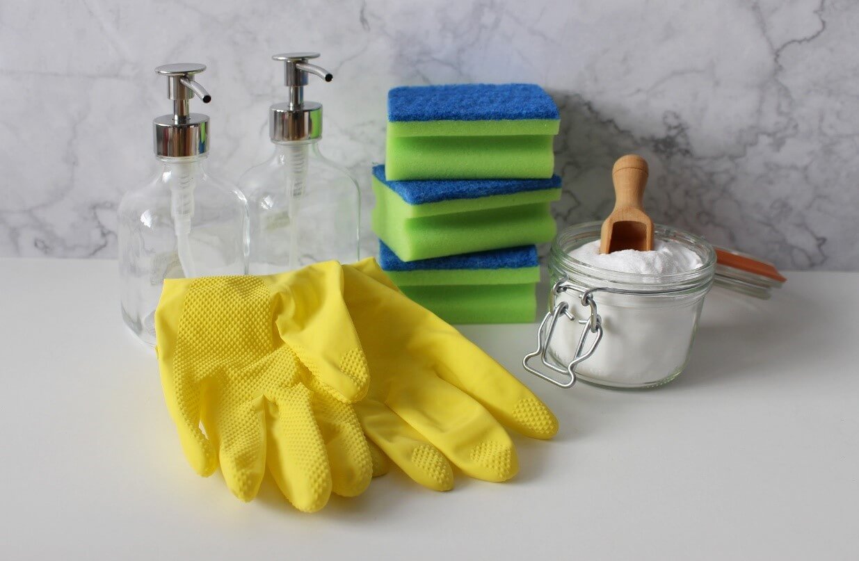 A white table with cleaning supplies including rubber gloves, a brush, and a powdered abrasive cleaner