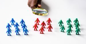 Magnifying glass above three groups of stick figures - blue, red and green.
